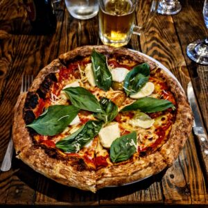 A delicious pizza topped with fresh basil leaves on a wooden table, with glasses of drinks in the background.